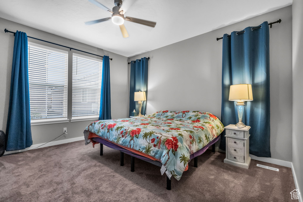 Bedroom with dark colored carpet, multiple windows, and ceiling fan