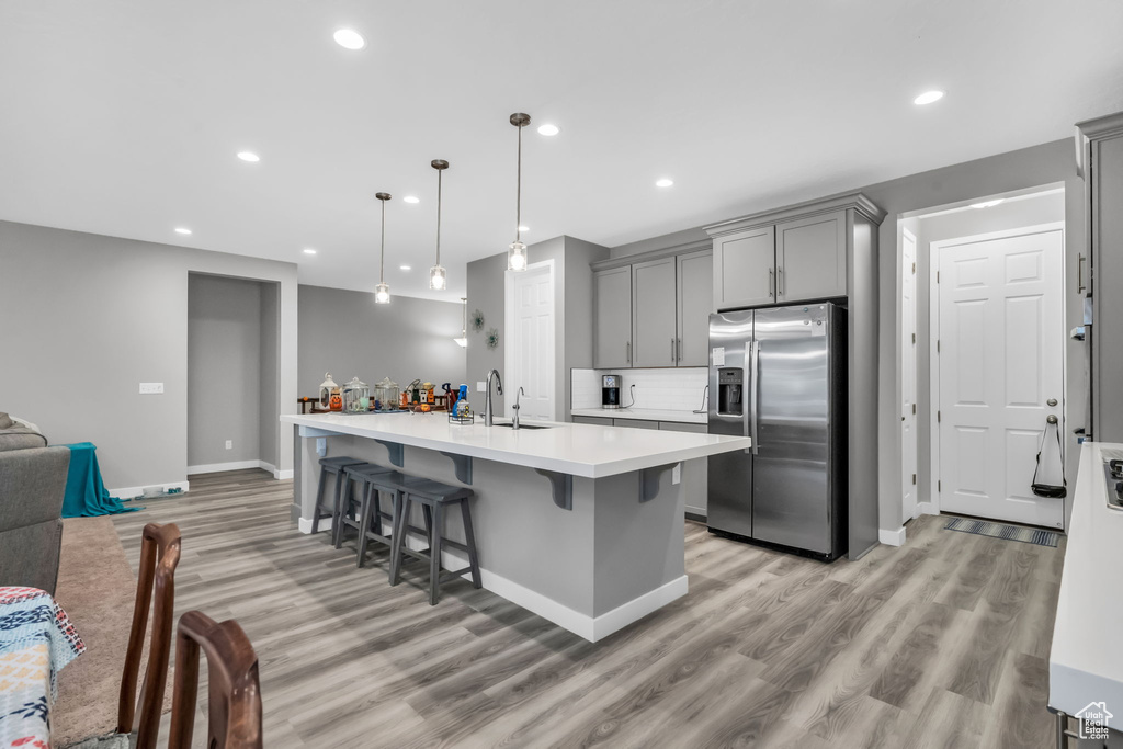 Kitchen with a kitchen breakfast bar, stainless steel fridge, gray cabinetry, and light hardwood / wood-style flooring