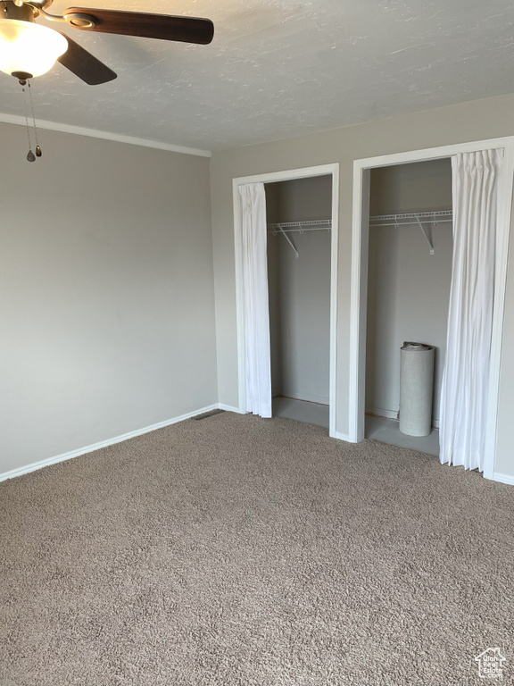 Unfurnished bedroom featuring ceiling fan, two closets, and carpet
