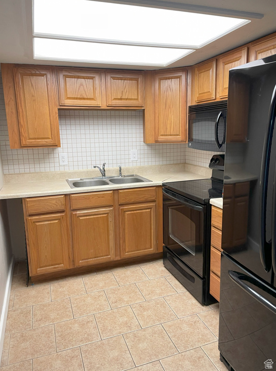 Kitchen with black appliances, backsplash, light tile flooring, and sink