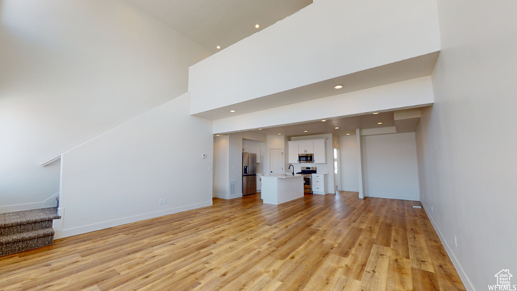 Unfurnished living room with a high ceiling, light hardwood / wood-style floors, and sink