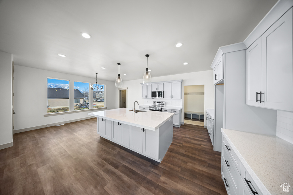 Kitchen featuring appliances with stainless steel finishes, a center island with sink, white cabinets, dark wood-type flooring, and pendant lighting