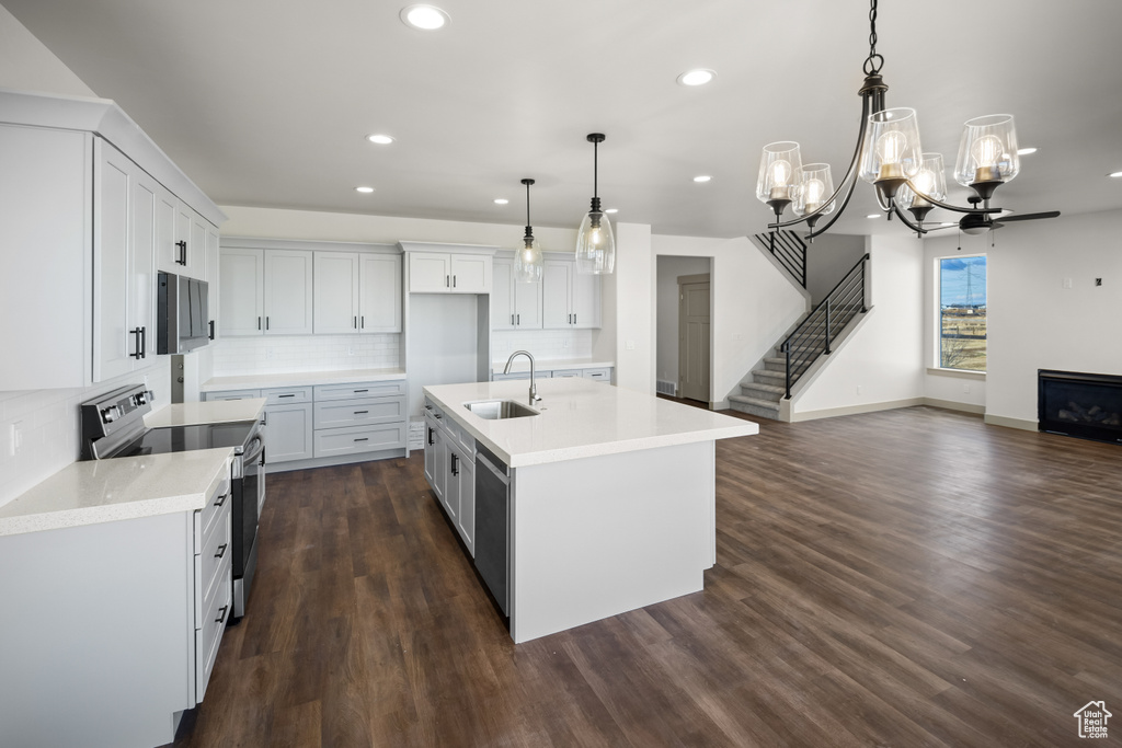 Kitchen featuring backsplash, a kitchen island with sink, dark hardwood / wood-style flooring, decorative light fixtures, and stainless steel electric range