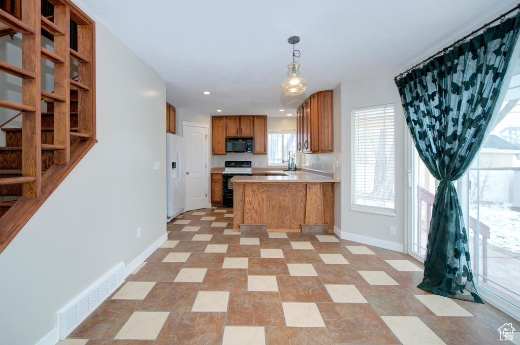 Kitchen with light tile floors, white appliances, kitchen peninsula, and decorative light fixtures