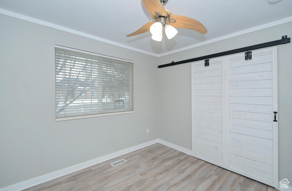 Unfurnished bedroom with a barn door, light wood-type flooring, a closet, and ceiling fan
