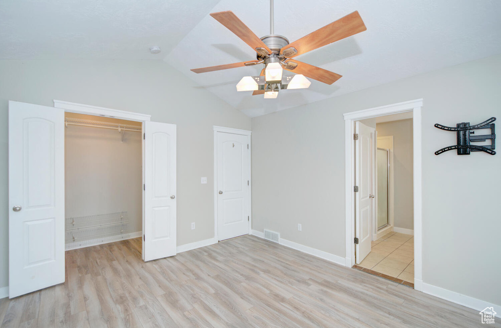 Unfurnished bedroom with light hardwood / wood-style flooring, lofted ceiling, connected bathroom, and ceiling fan
