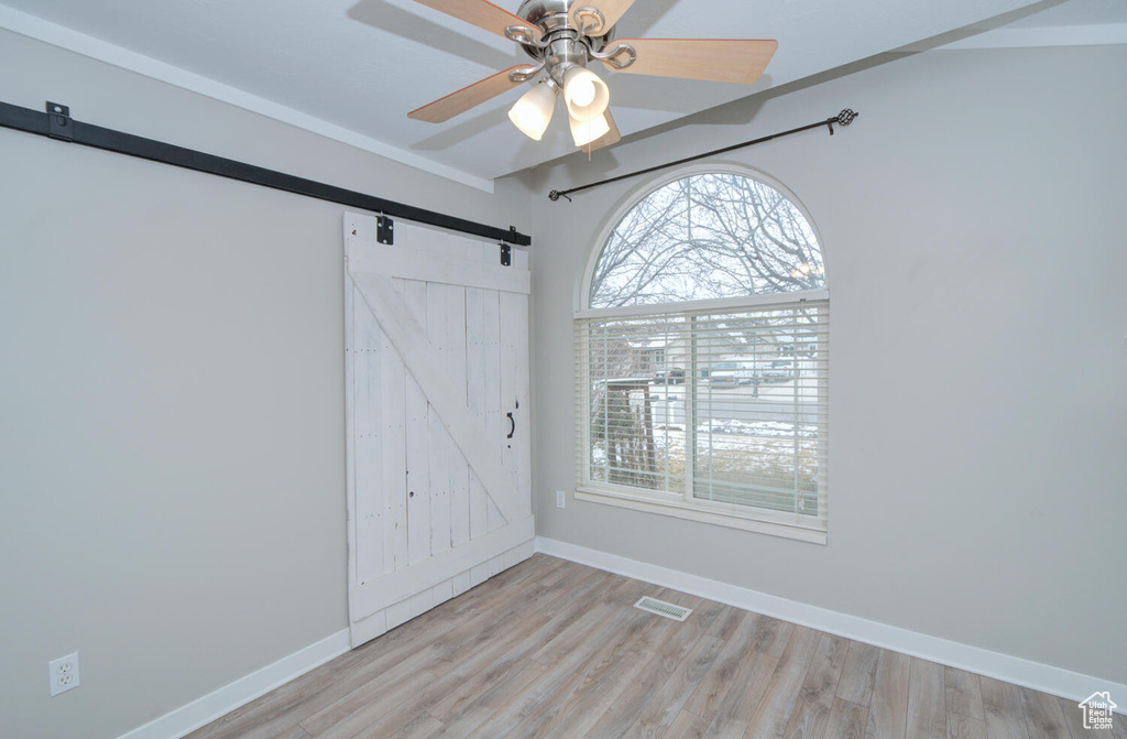 Spare room featuring ceiling fan, light hardwood / wood-style floors, and a barn door