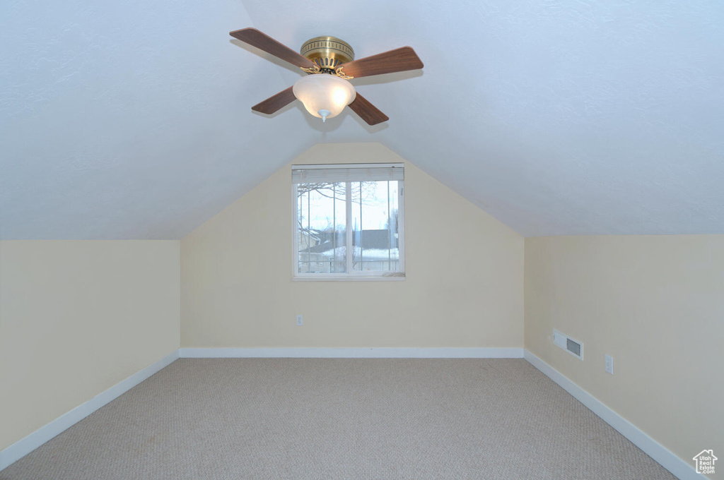 Additional living space featuring light colored carpet, lofted ceiling, and ceiling fan