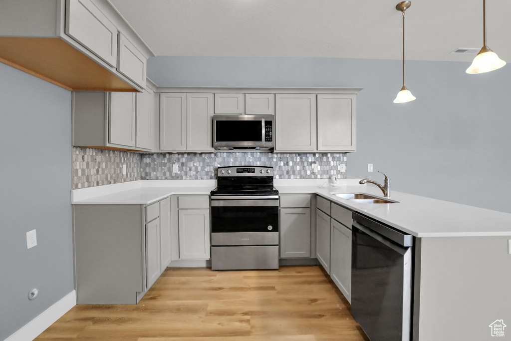 Kitchen featuring sink, pendant lighting, light wood-type flooring, kitchen peninsula, and stainless steel appliances