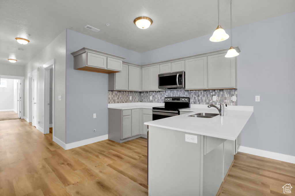 Kitchen with sink, kitchen peninsula, decorative light fixtures, appliances with stainless steel finishes, and light wood-type flooring