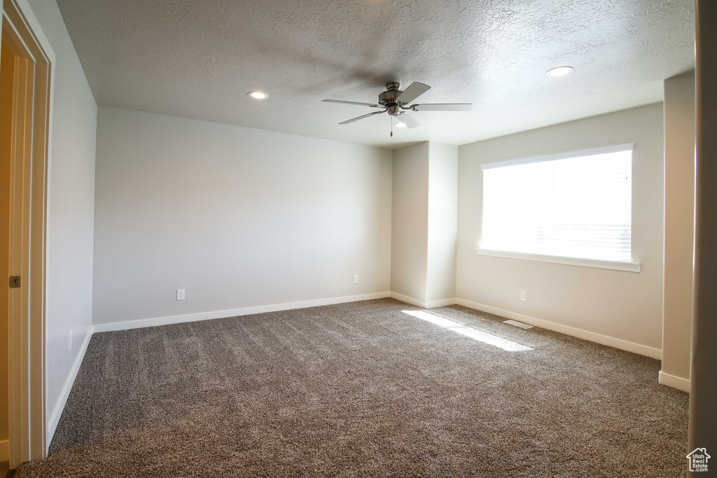 Unfurnished room featuring dark colored carpet, ceiling fan, and a textured ceiling