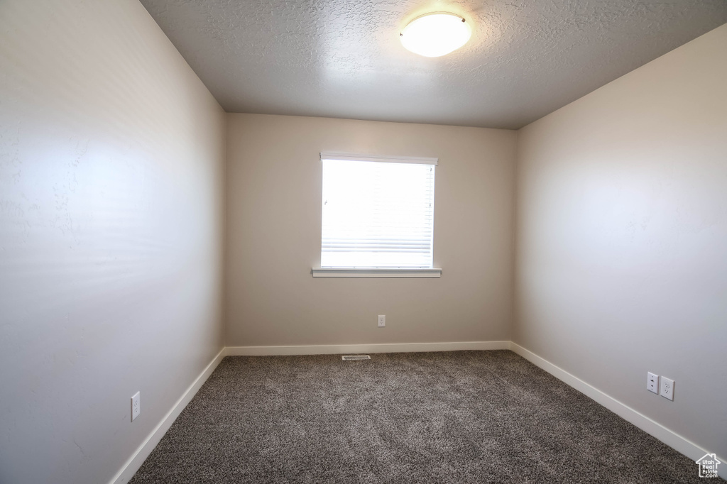 Unfurnished room with a textured ceiling and dark carpet