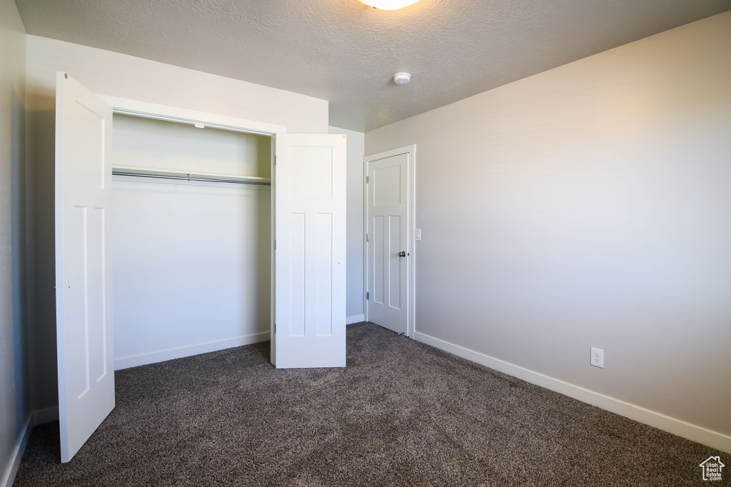 Unfurnished bedroom with a textured ceiling, a closet, and dark colored carpet