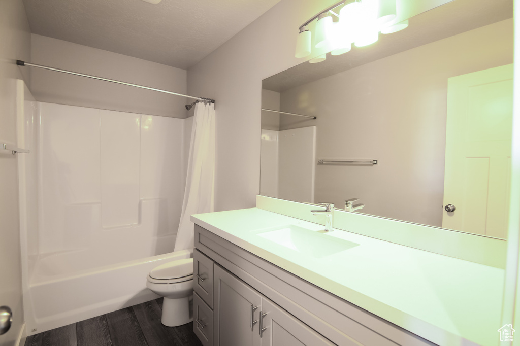 Full bathroom featuring toilet, shower / bathtub combination with curtain, vanity with extensive cabinet space, and hardwood / wood-style flooring