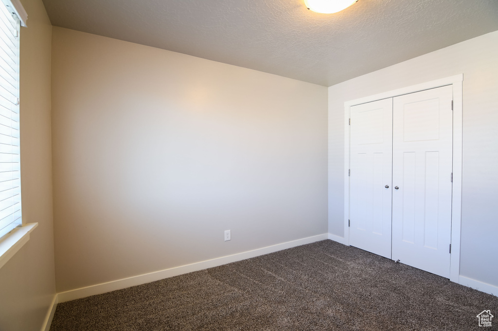 Unfurnished bedroom featuring a textured ceiling, dark colored carpet, and a closet