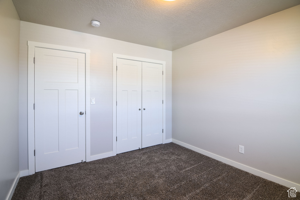 Unfurnished bedroom with a textured ceiling, dark carpet, and a closet