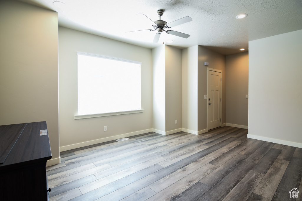 Empty room with ceiling fan, a textured ceiling, and light hardwood / wood-style flooring