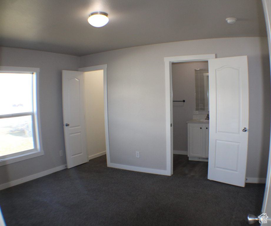 Unfurnished bedroom with a closet, connected bathroom, and dark carpet