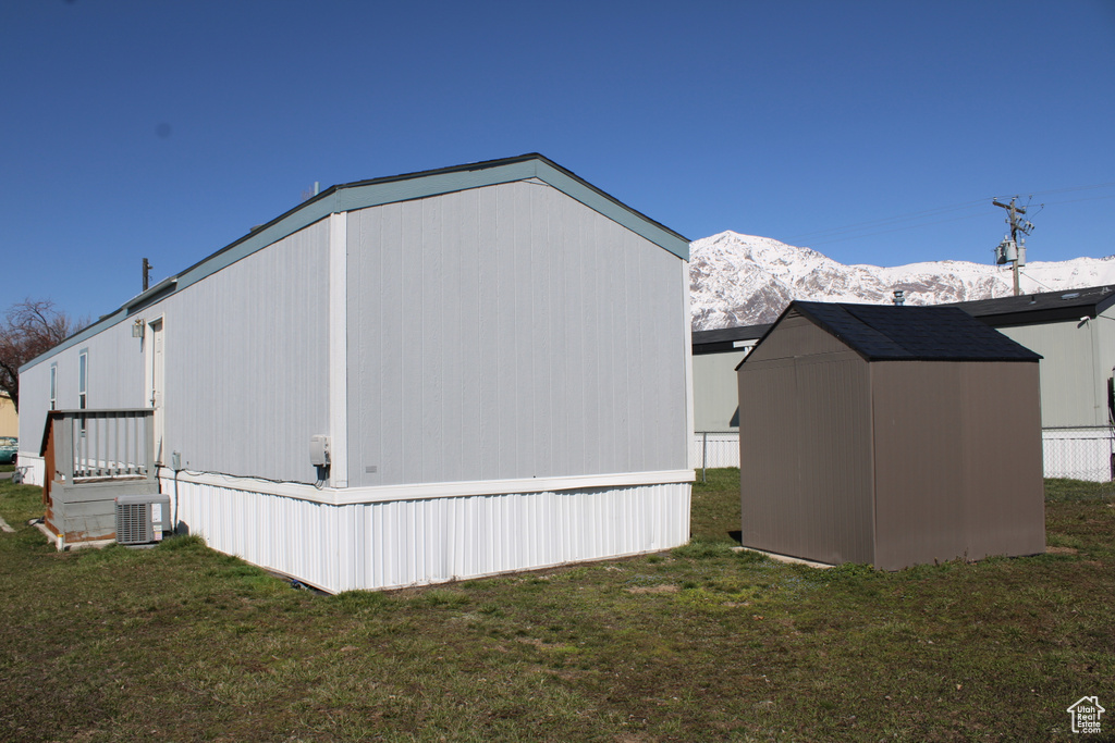 View of side of property featuring a shed, central AC, a yard, and a mountain view