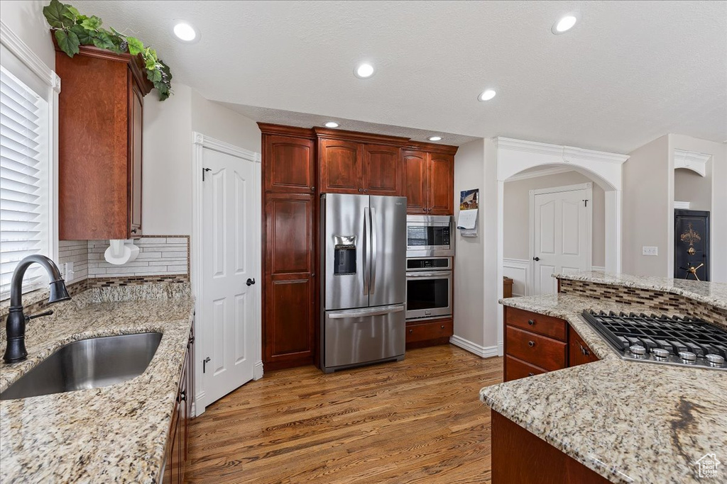 Kitchen featuring sink, tasteful backsplash, dark hardwood / wood-style flooring, appliances with stainless steel finishes, and light stone counters
