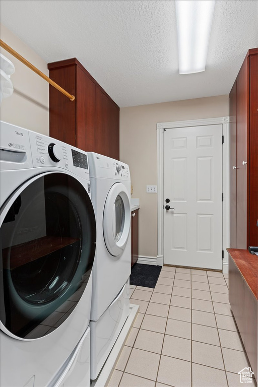 Laundry room featuring cabinets, washer and clothes dryer, a textured ceiling, and light tile floors