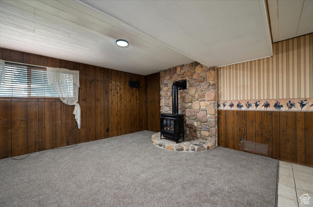 Unfurnished living room featuring light colored carpet, wood walls, and a wood stove