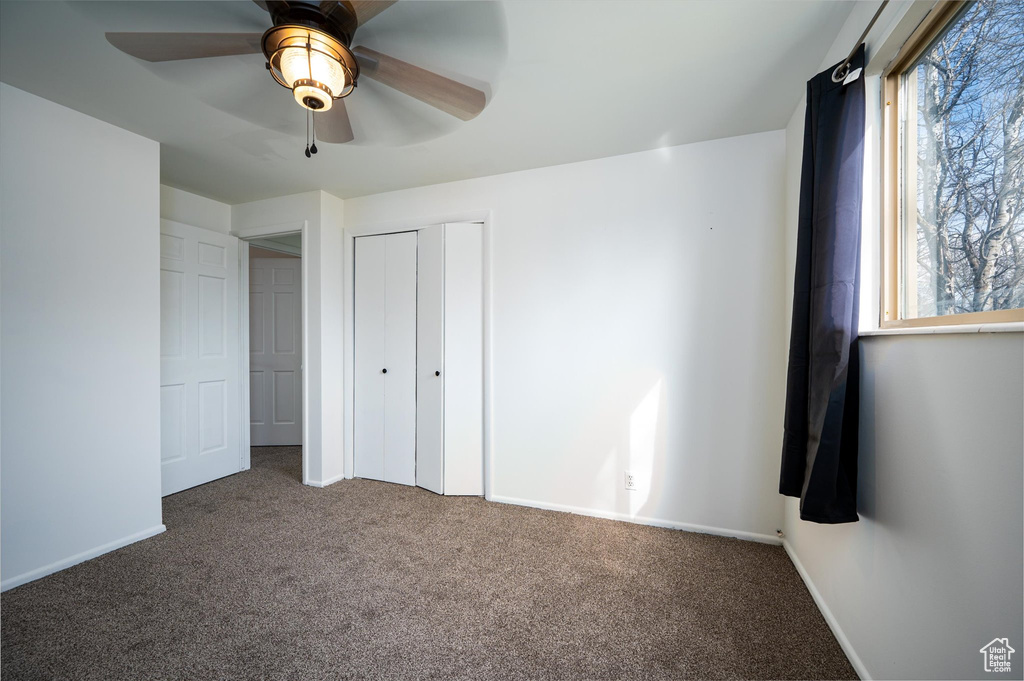 Unfurnished bedroom with dark colored carpet, multiple windows, and ceiling fan