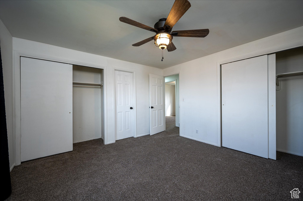 Unfurnished bedroom featuring dark colored carpet, ceiling fan, and two closets