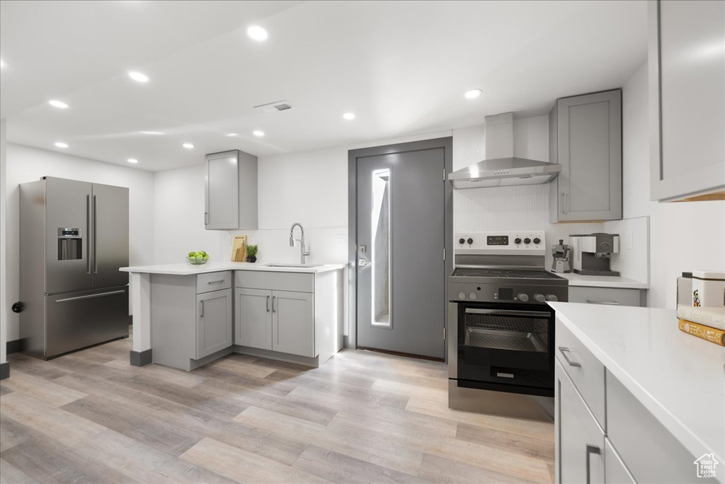 Kitchen with gray cabinetry, appliances with stainless steel finishes, sink, light hardwood / wood-style flooring, and wall chimney exhaust hood