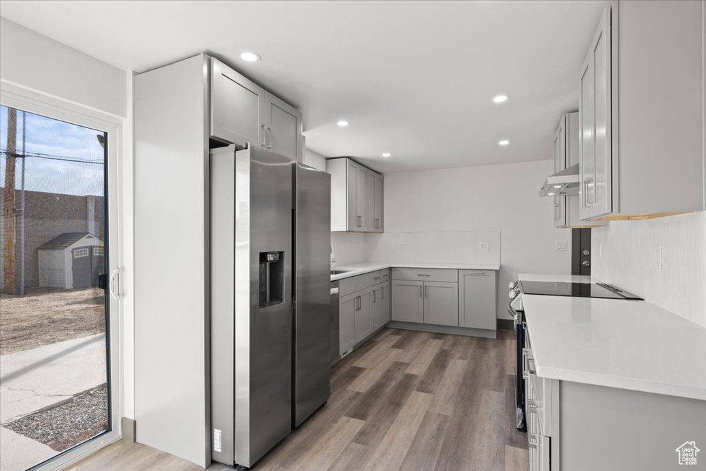 Kitchen featuring wall chimney range hood, stainless steel fridge with ice dispenser, light hardwood / wood-style floors, and gray cabinetry