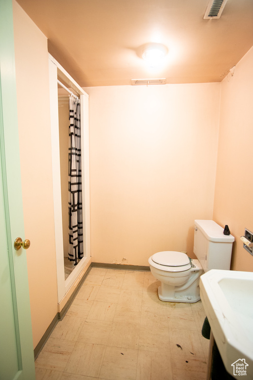 Bathroom with toilet, a shower with shower curtain, and tile floors