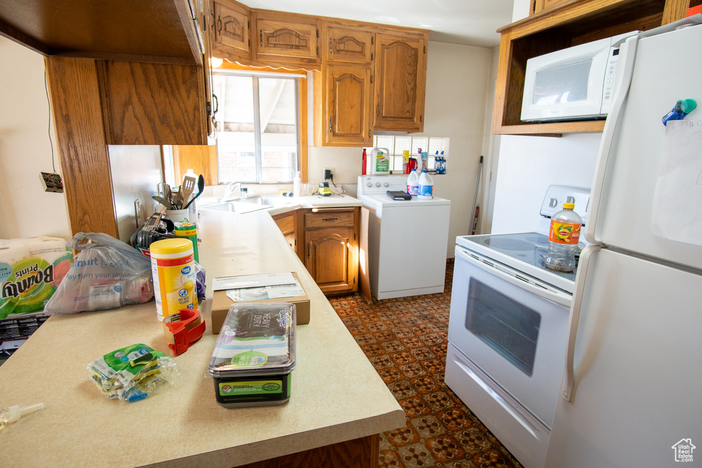 Kitchen with washer / dryer, white appliances, dark tile floors, and sink