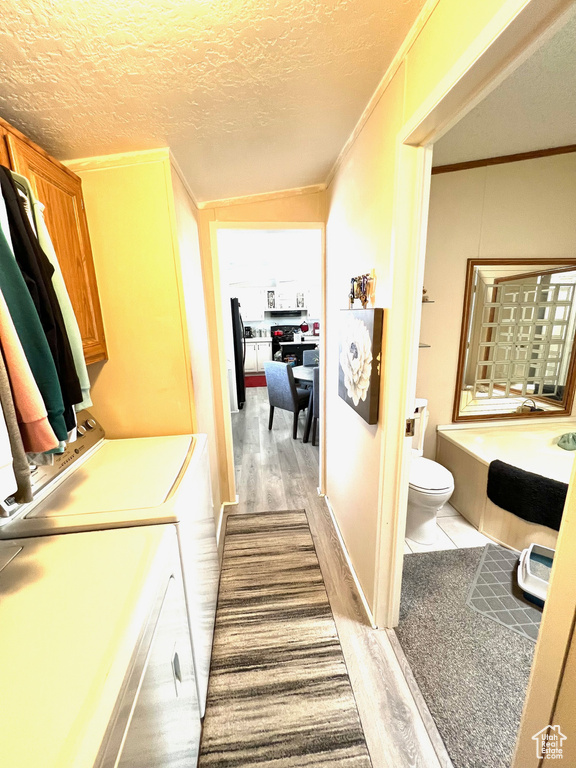 Washroom with a textured ceiling, ornamental molding, light hardwood / wood-style floors, and washer and dryer