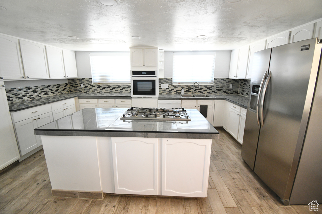 Kitchen featuring white cabinets, light hardwood / wood-style floors, stainless steel appliances, and a center island