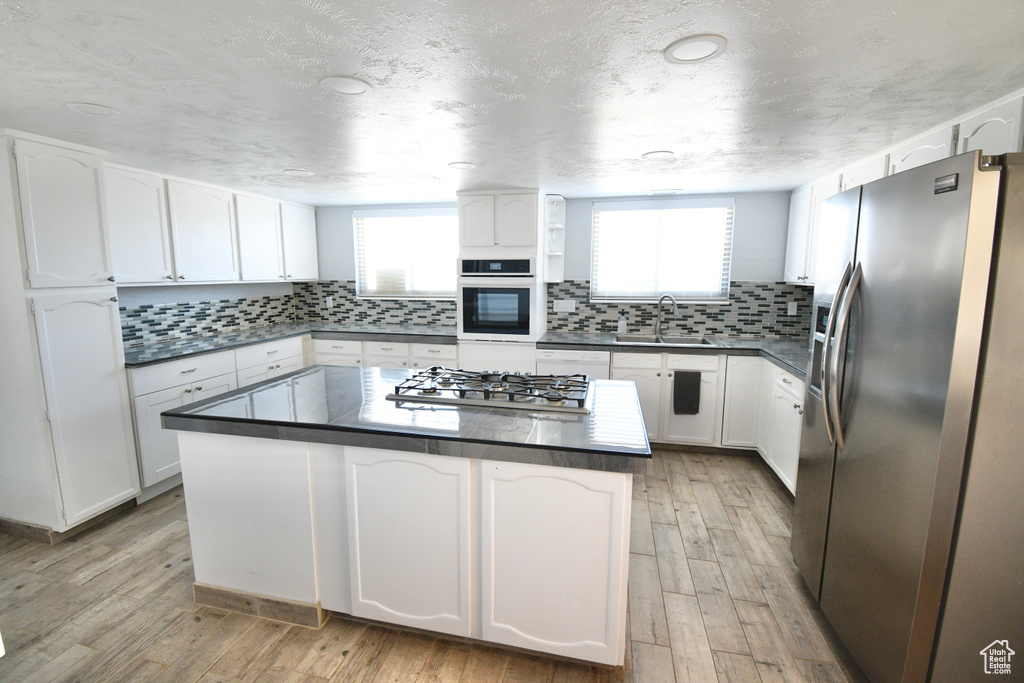 Kitchen with plenty of natural light, white cabinets, appliances with stainless steel finishes, and light hardwood / wood-style flooring