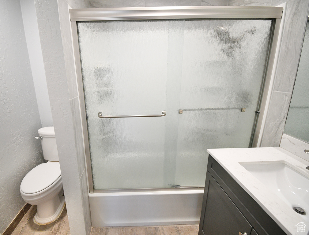Full bathroom featuring wood-type flooring, shower / bath combination with glass door, vanity, and toilet