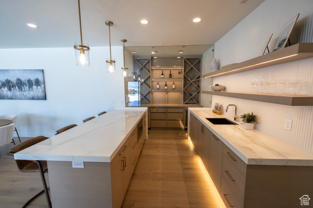 Kitchen featuring a kitchen island, sink, light hardwood / wood-style floors, a kitchen breakfast bar, and hanging light fixtures