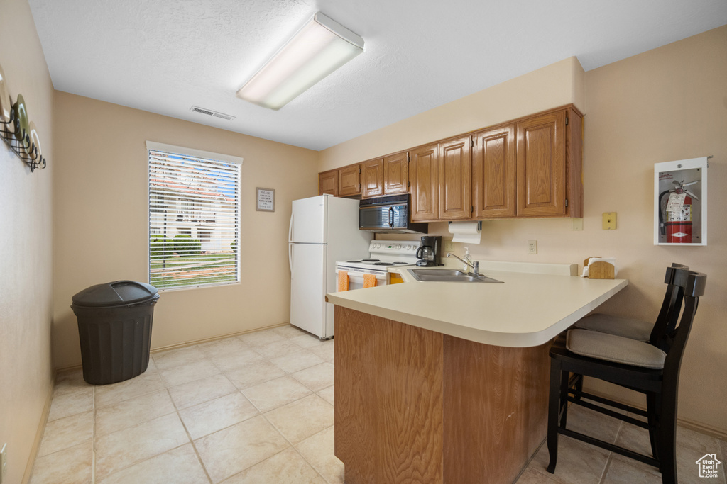 Kitchen featuring a kitchen breakfast bar, sink, white appliances, kitchen peninsula, and light tile floors
