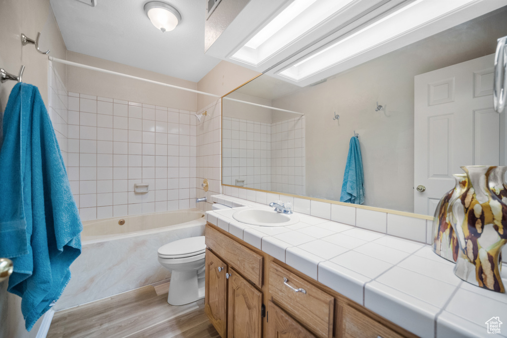 Full bathroom featuring toilet, vanity with extensive cabinet space, wood-type flooring, and tiled shower / bath combo