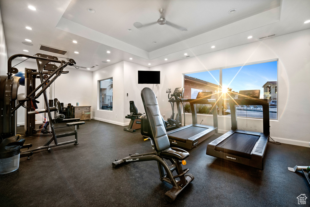 Workout area with ceiling fan with notable chandelier and a tray ceiling