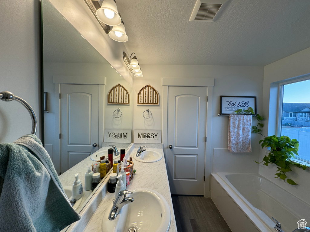 Bathroom featuring a bathtub, a textured ceiling, hardwood / wood-style floors, double sink, and large vanity