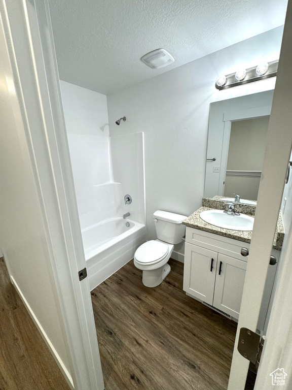 Full bathroom with a textured ceiling, shower / tub combination, hardwood / wood-style floors, oversized vanity, and toilet