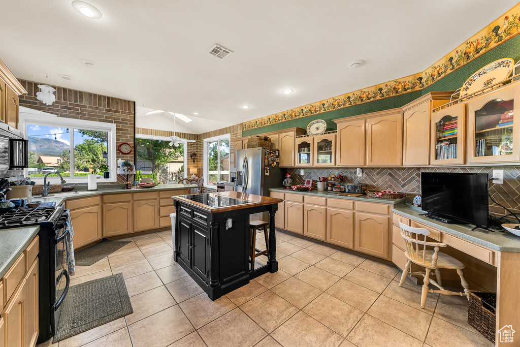 Kitchen with light tile flooring, range with gas cooktop, stainless steel refrigerator with ice dispenser, backsplash, and a kitchen island
