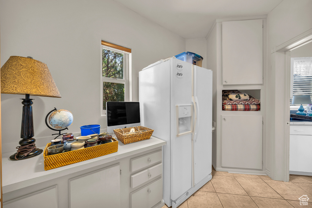 Kitchen with white cabinetry, white fridge with ice dispenser, and light tile flooring