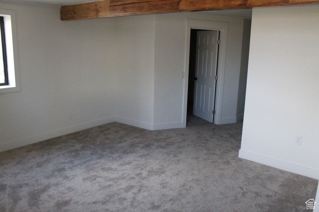 Spare room featuring beamed ceiling and dark colored carpet