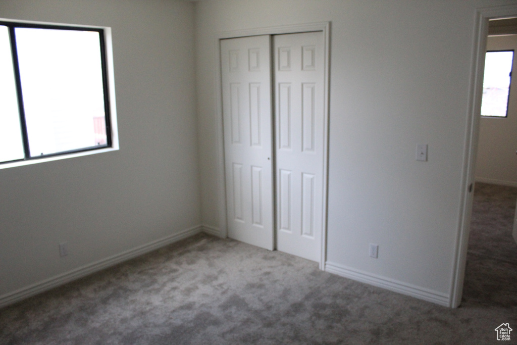 Unfurnished bedroom with dark colored carpet, multiple windows, and a closet