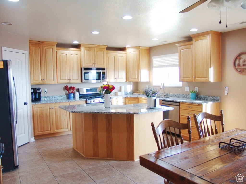Kitchen featuring a kitchen island, stainless steel appliances, ceiling fan, and light stone countertops