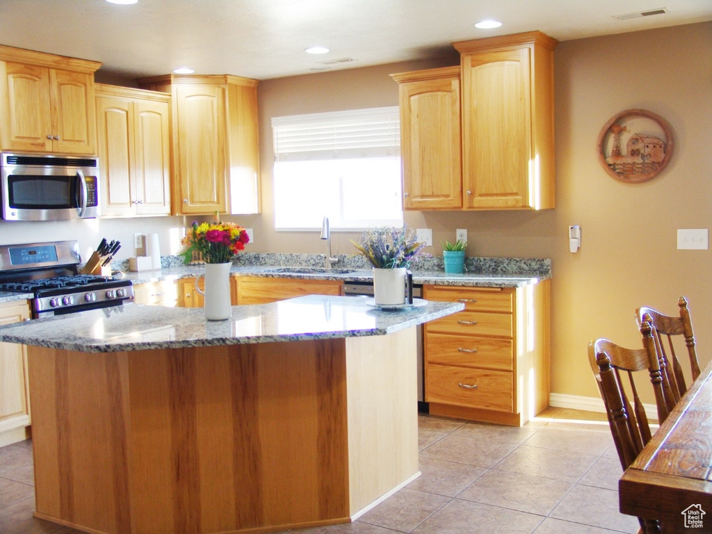 Kitchen with light tile flooring, appliances with stainless steel finishes, light stone countertops, and sink