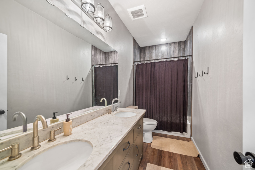 Bathroom featuring vanity with extensive cabinet space, hardwood / wood-style flooring, toilet, and double sink
