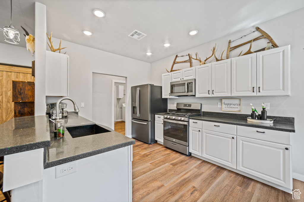 Kitchen with decorative light fixtures, white cabinetry, stainless steel appliances, and light hardwood / wood-style floors
